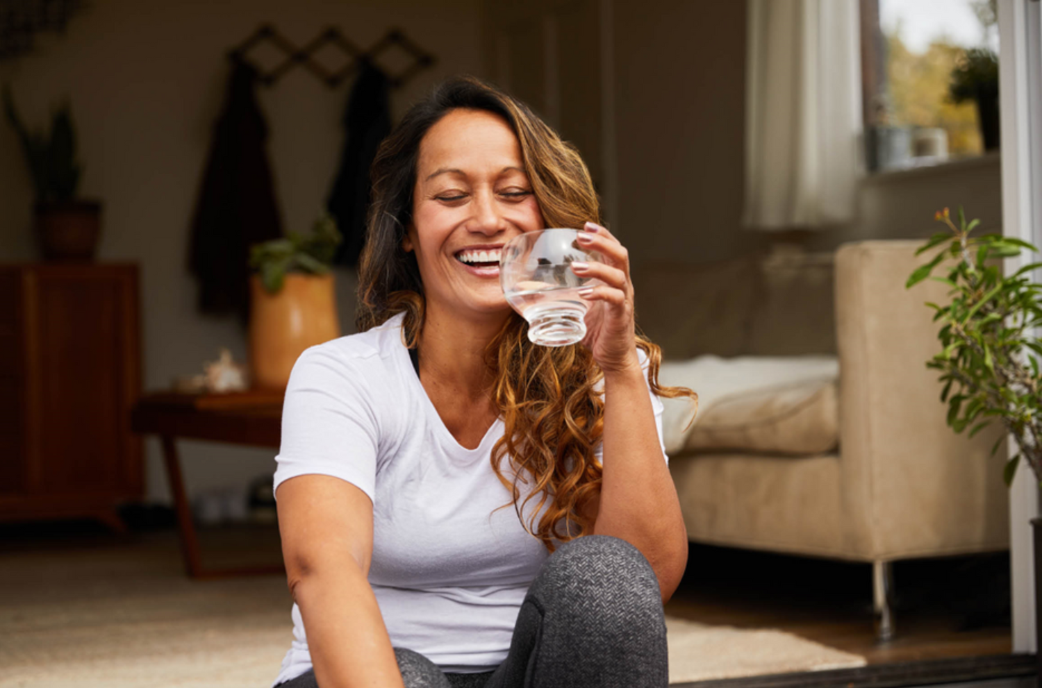 A lady sitting out with a glass cup eye closed and laughing