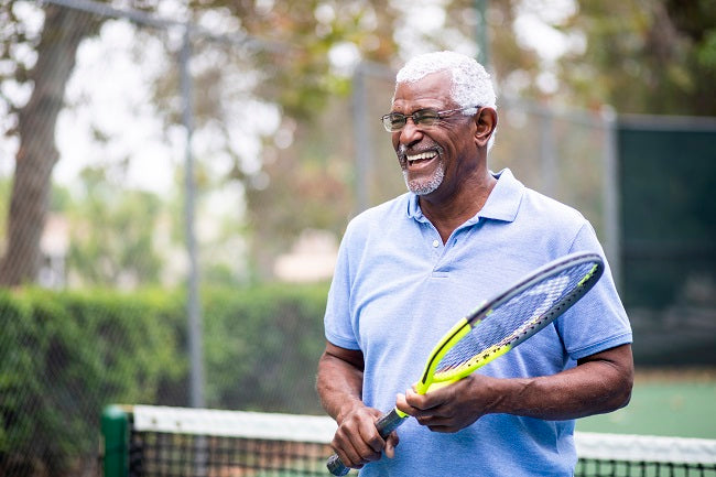 Un senior met des verres progressifs et se tient debout sur le court de tennis avec une raquette à la main.