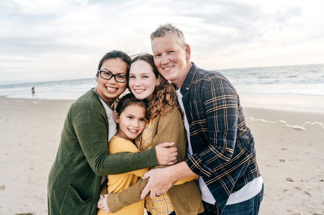 Une famille de 4 personnes debout au bord de la plage. La femme met des lunettes.