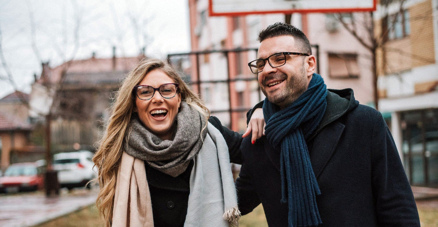 Un couple marche dans la rue et sourit. Ils portent tous les deux des lunettes avec de superbes verres